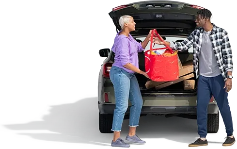 A woman in a periwinkle pullover hands a red bag of groceries to her spouse.